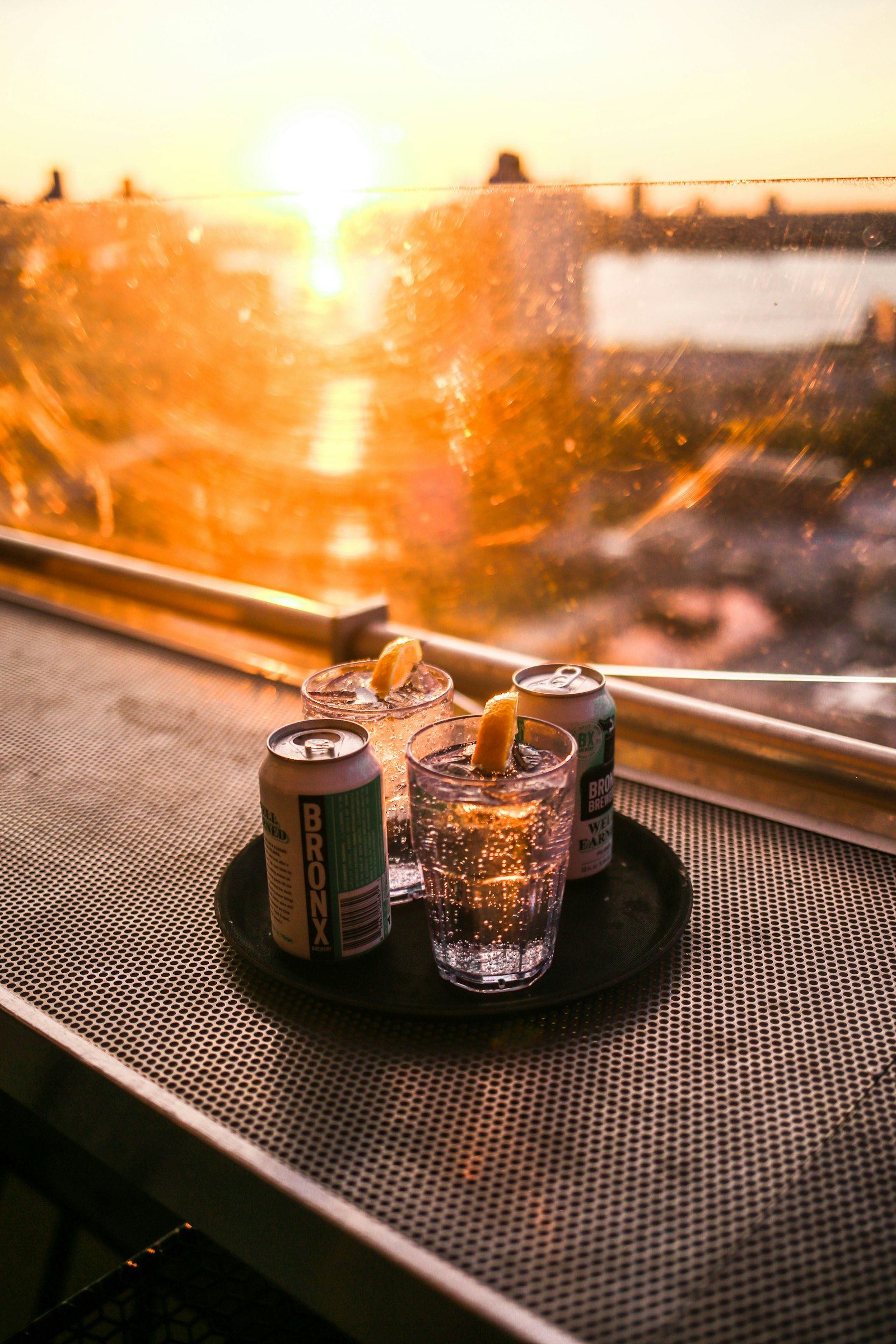 Cocktails on a tray at the rooftop railing as the sun sets over the water
